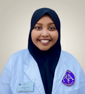 Headshot of Sumaya Noor smiling at the camera. She is wearing a white lab coat and dark headscarf.